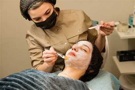 A close-up of a facial treatment, showing an esthetician applying a mask to a client's face.