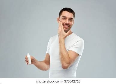 Close-up photo of a man applying body lotion to his skin.