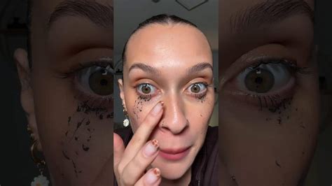 A close-up shot of a person gently removing tubing mascara from their lashes with a cotton pad and warm water.