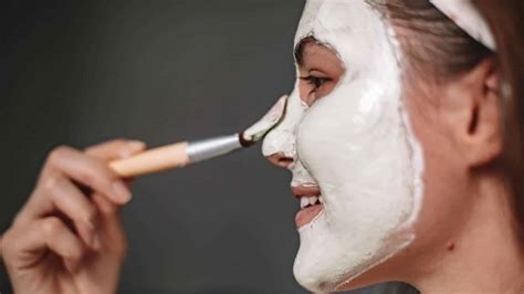 A person applying white face paint evenly across their face with a sponge, creating a smooth, opaque base.