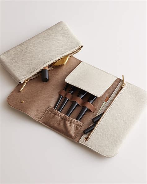 A luxurious leather travel beauty roll from Cuyana, partially open to show its compartments.