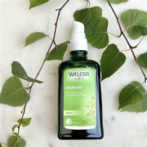 Product shot of Weleda Birch Cellulite Oil bottle alongside fresh birch leaves and a citrus fruit.
