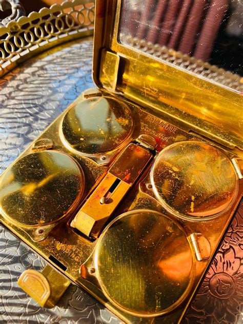 An ornate vintage makeup compact, showcasing intricate metalwork and inlaid stones, representing the artistry of early 20th-century cosmetic accessories.