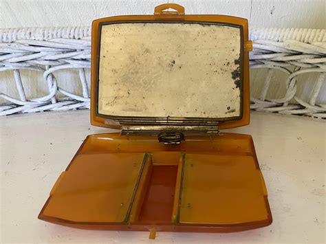 An open vintage compact revealing its interior compartments for lipstick, powder, and a mirror, demonstrating the thoughtful functionality of these accessories.