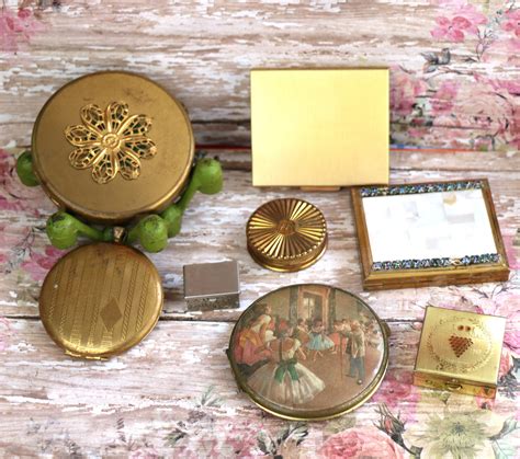 A display of various vintage compacts, including bakelite, brass, and silver examples, illustrating the range of materials and price points available to collectors.