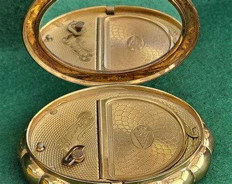 A vintage Kigu advertisement showcasing their elaborate powder compacts, highlighting the brand's reputation in the mid-20th century.
