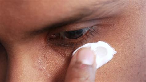 Close-up photo showing a person applying an under-eye cream with a cooling applicator.
