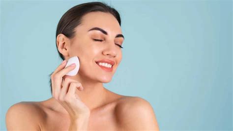 A makeup artist demonstrating the application of foundation with a damp beauty sponge.