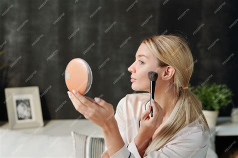 A woman applying setting powder to her face with a large brush.