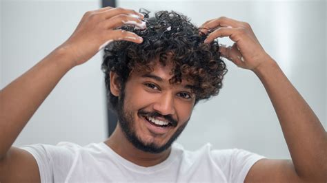 A man with curly hair applying a hair product.