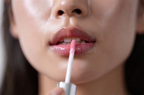 A person applying a plumping lip gloss, showing a subtle color and fuller-looking lips.