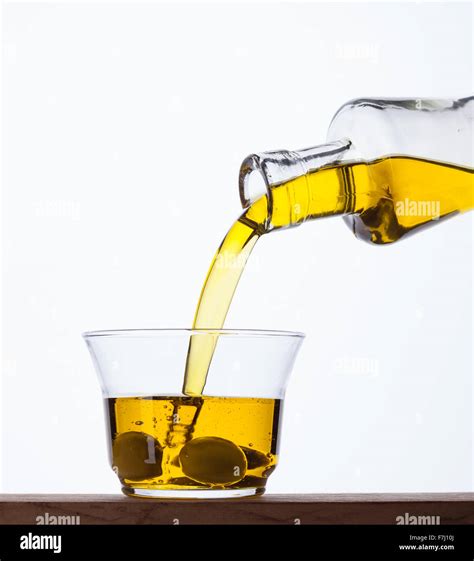 Close-up image of olive oil being poured into a glass, with a bowl of grapefruit nearby.