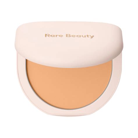 A close-up of the Rare Beauty Soft Touch Powder Puff and the compact powder in its half-moon shaped packaging.