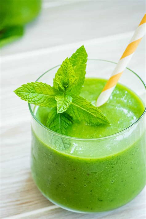 A vibrant green smoothie in a glass, garnished with a mint leaf and a few fruit slices.