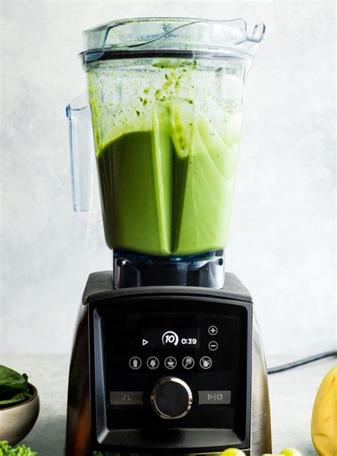 A close-up of a blender filled with green smoothie ingredients before blending.