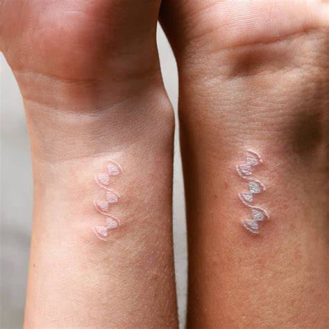 A delicate white ink tattoo design on dark skin, showcasing its subtle appearance.