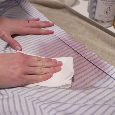 Close-up of someone blotting a foundation stain on white fabric with a paper towel