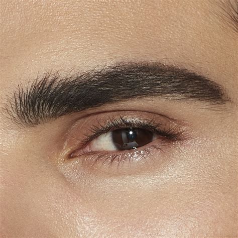 Close-up of a man's eyebrows being groomed with a pencil and spoolie.