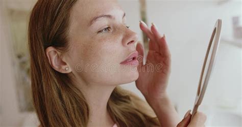 A woman looking at her reflection in a mirror, examining her skin.
