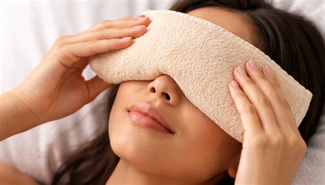 Close-up of a person applying a warm compress to their closed eye.