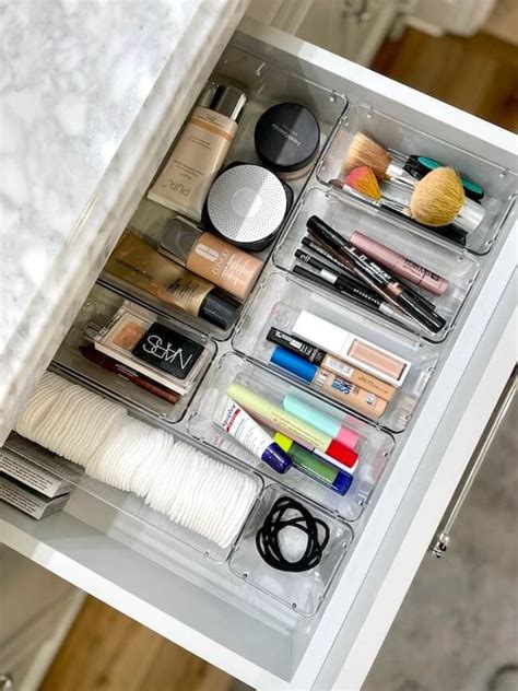 An organized makeup drawer with various clear organizers filled with different beauty products.