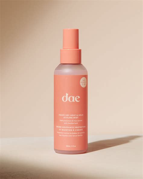 A person spraying Dae Agave Dry Heat & Hold Styling Mist onto their hair before using a curling iron.