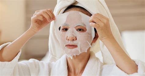 Close-up shot of a person applying a chilled sheet mask from a skincare fridge to their face.