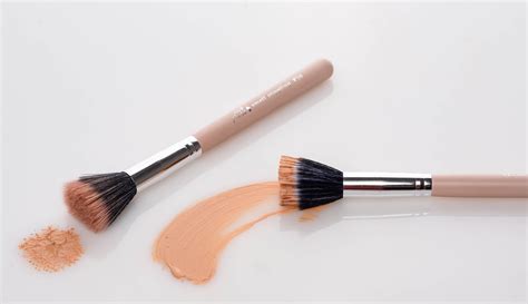 Close-up of a stippling brush showing its dual-layer bristles and a swatch of foundation applied with it.