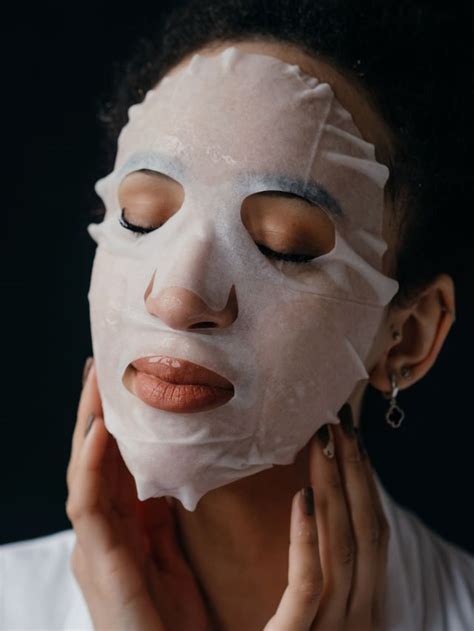 A close-up photo of a person applying a sheet mask to their face, showcasing the product's texture and application.