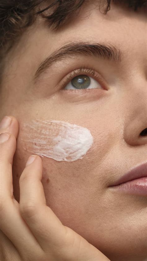 Close-up of a finger gently dabbing cream blush onto the cheekbone.