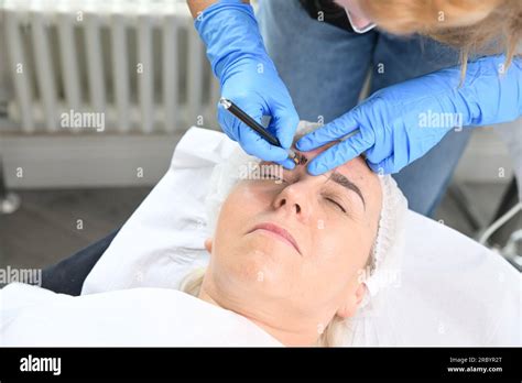 Close-up photo of an artist's hands performing microblading on an eyebrow, showing the precision tool and pigment.