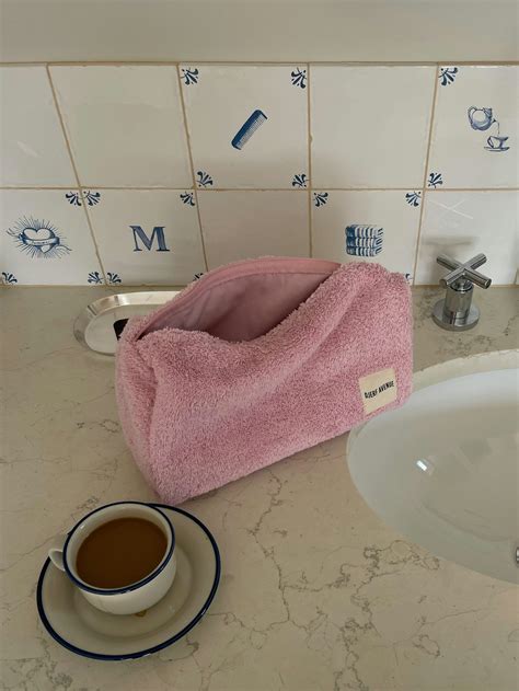 Illustration of the Djerf Avenue Terry Beauty Bag in various colors, highlighting its organic cotton material and dimensions.