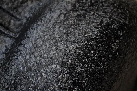 A close-up of a car engine component coated with textured black wrinkle paint, highlighting its unique finish and durability.