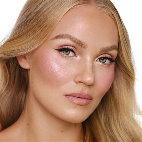 A model with a sun-kissed, glowy makeup look featuring bright pink blush on cheeks and nose, and highlighter on the high points of the face.