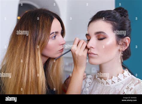 A makeup artist applying eyeliner to a model's eye.