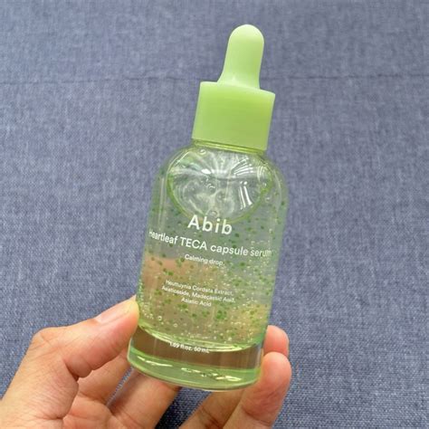 A clear glass bottle with a dropper, showcasing a light green serum inside, with the Abib Heartleaf branding.