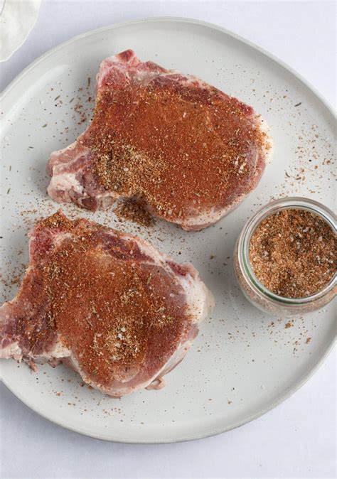 Close-up of a pork shoulder being seasoned with a mixture of herbs and spices, with deep slits visible.