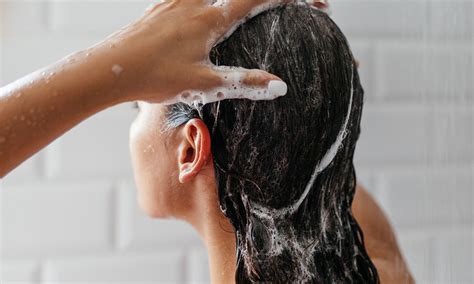 A person using a scalp massager in the shower while shampooing their hair.